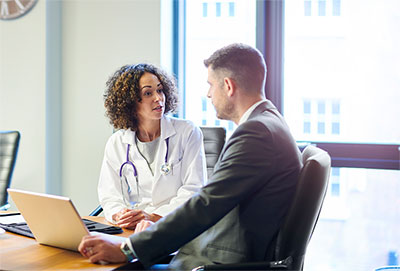 Physician talking with a business person at a desk.