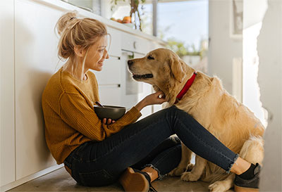 Young woman sitting in the kitchen scratching her dog.