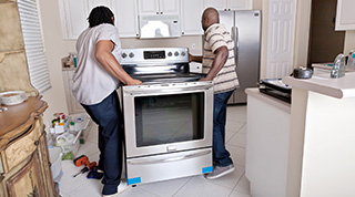 Couple moving stove into kitchen.