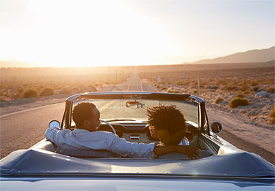 A young couple driving down a desert highway in a convertible.