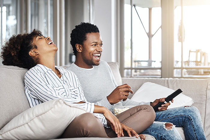 Young couple on couch laughing while watching tv.