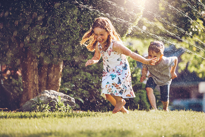 Two children playing in sprinklers.