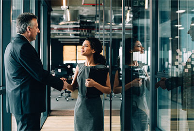 Businessman and woman shaking hands in office corridor.